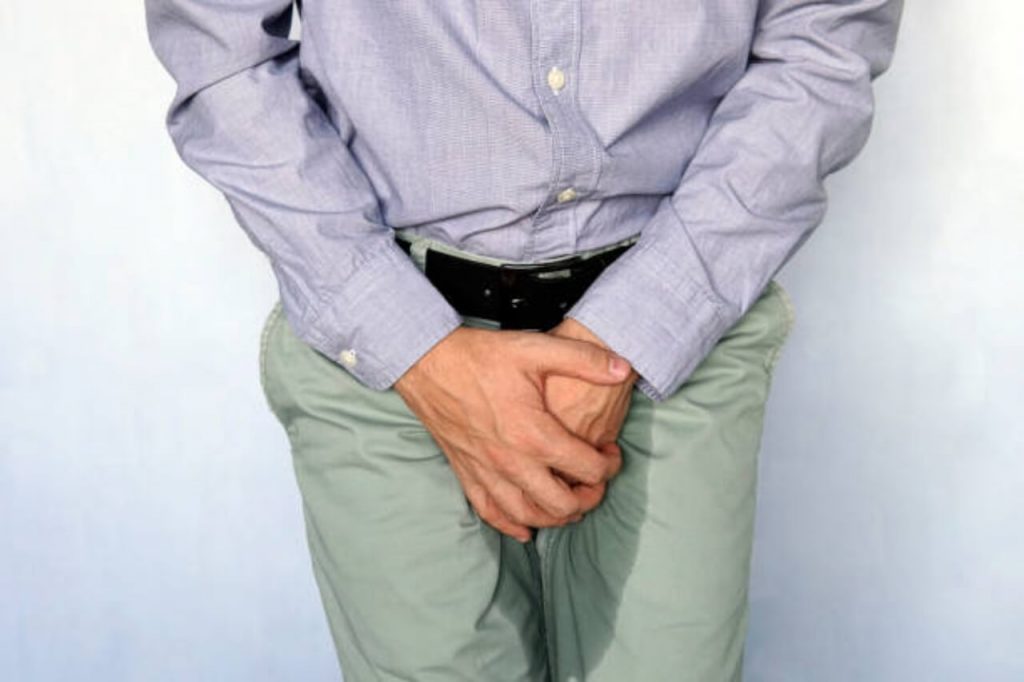Hombre tiene las manos en la zona pélvica y su pantalón está mojado, padece uno de los síntomas de la incontinencia urinaria, la pérdida involuntaria de orina