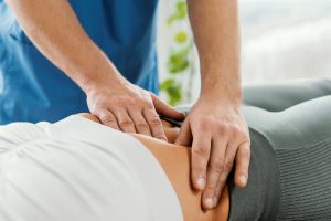 Mujer acostada en la camilla mientras el profesional de la salud presiona el área del abdomen haciendo terapias para fortalecer el suelo pélvico