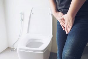 Imagen de mujer en un baño ella está colocando sus manos en la zona pélvica como con dolor con infecciones urinarias